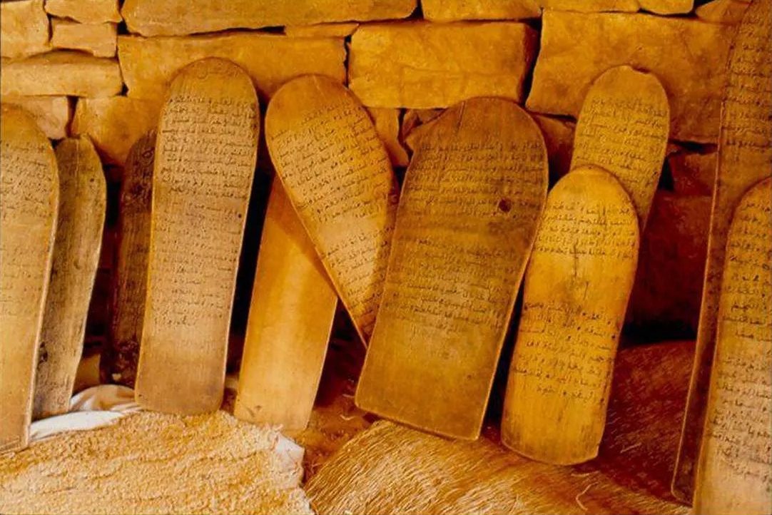 ألواح خشبية كُتبت عليها المتون بخط اليد، مسنَدة إلى جدار حجري في محظرة شنقيطية
